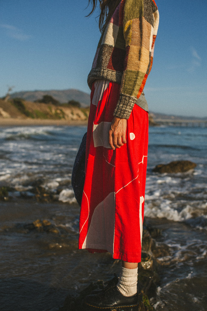 The Christmas Skirt, a vibrant red skirt features bold white patches and intricate appliqué needlework, combining comfort and style in a standout design