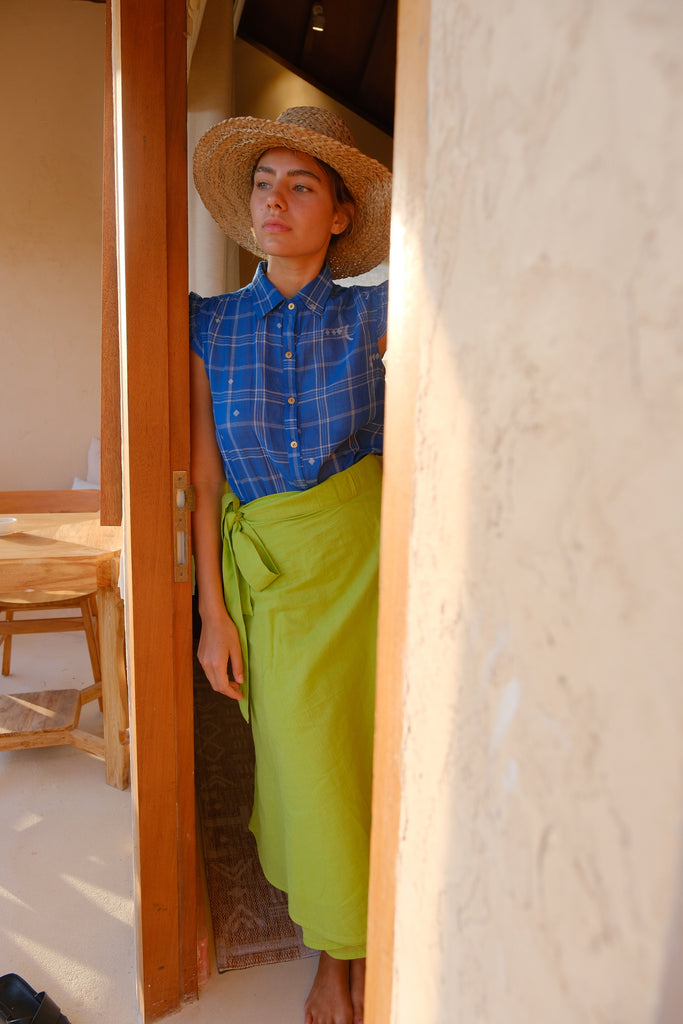 Discover effortless elegance with our hand-woven cotton wrap skirt, showcased in a vibrant parrot green. A woman models this summer-ready piece, paired with a chic hat, illustrating its ideal blend of style and sustainability. Crafted with care for environmentally-conscious fashion lovers, this midi-length skirt is perfect for embracing the sunny season in sustainable sophistication