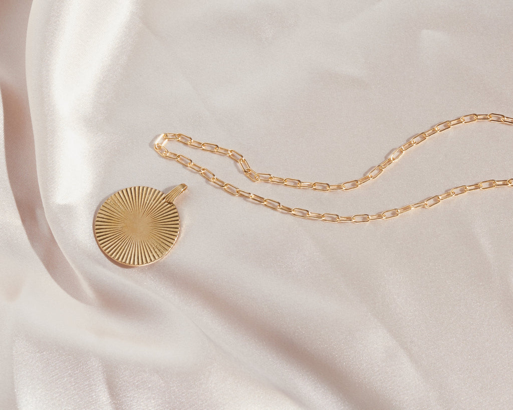 Introducing the Vintage-Inspired Gold Sunburst Pendant Necklace. This elegant gold disc features a sunburst design, gracefully suspended from a 21" chain. Choose between a 14K Gold Plated Curb Chain or a 14K Gold Filled Link Chain for a touch of customizable sophistication.