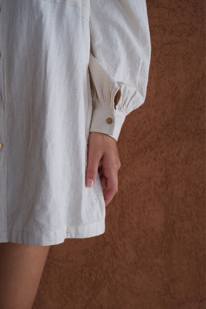 Introducing the White Artist Smock, a collaboration between Audrey E Leary and World of Crow. This short-length smock, crafted from thick, handwoven organic cotton, features a straight collar, puff full sleeves, and gathered cuffs. With spacious pockets and a comfortable fit, it's ideal for painting, crafting, and staying cozy during travel.