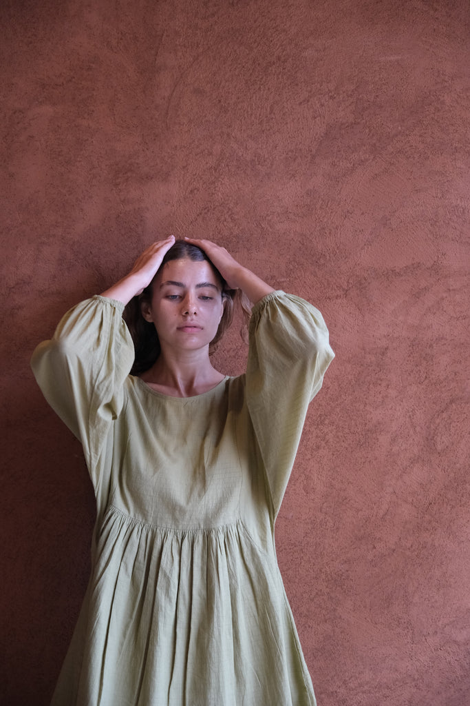 Introducing the Olive Get Away Dress, a collaboration between Audrey E Leary and World of Crow. This mini dress in unique olive green features a scoop neck and three-quarter puff sleeves, crafted from soft, handwoven cotton. Sustainably made and breathable, it offers a comfortable, true-to-size fit with lightweight, non-stretchy fabric, ideal for everyday wear.