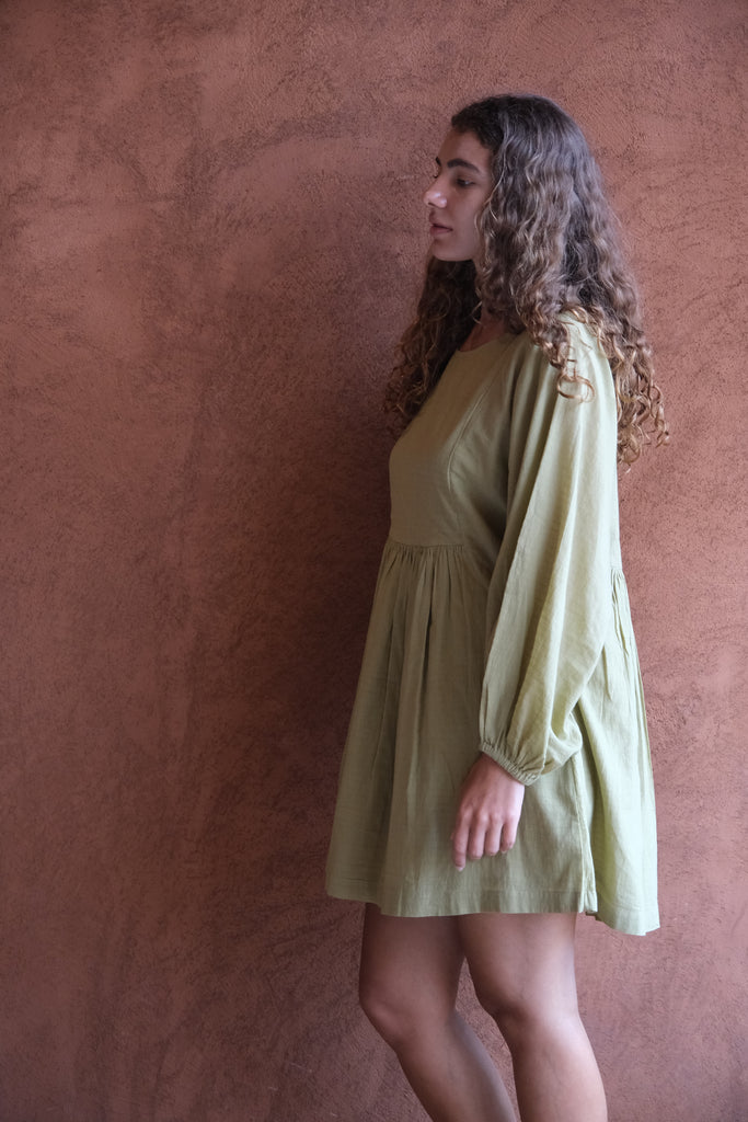 Introducing the Olive Get Away Dress, a collaboration between Audrey E Leary and World of Crow. This mini dress in unique olive green features a scoop neck and three-quarter puff sleeves, crafted from soft, handwoven cotton. Sustainably made and breathable, it offers a comfortable, true-to-size fit with lightweight, non-stretchy fabric, ideal for everyday wear.