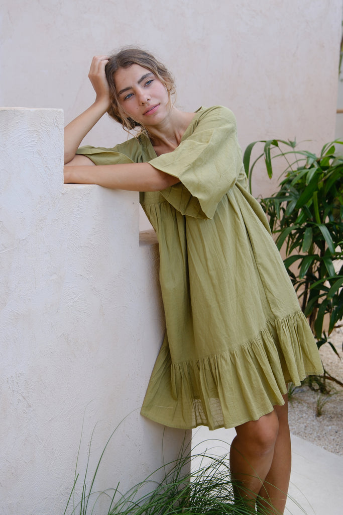 Introducing our Olive Green Day Dress by Audrey E Leary and World of Crow. This mini-length dress features a V-neck, drop shoulders, and a unique olive green color. Made from soft, handwoven cotton, it offers a comfortable, lightweight fit perfect for everyday wear