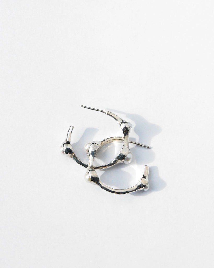 Introducing our elegant silver hoop earrings, featuring a sophisticated asymmetrical design with white pearls in varying sizes—3 mm, 4 mm, and 5 mm. Handcrafted with precision, these earrings are adorned with sterling silver posts and backs. Each pair is made to order and ships in 2-4 weeks, ensuring a unique addition to your collection.