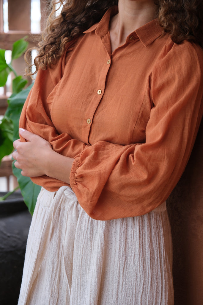 Introducing the Audrey X Crow Collection, featuring a woman in an orange Jane Austen Shirt and white skirt. This collection showcases hand-woven fabric with block-printed stripes, embodying elegance and artisanal craftsmanship. The vibrant orange and classic white combination adds a touch of sophistication to this beautifully crafted ensemble.