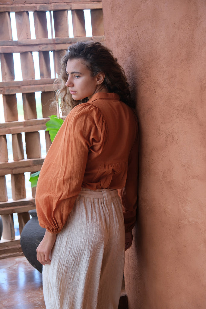 Introducing the Audrey X Crow Collection, featuring a woman in an orange Jane Austen Shirt and white skirt. This collection showcases hand-woven fabric with block-printed stripes, embodying elegance and artisanal craftsmanship. The vibrant orange and classic white combination adds a touch of sophistication to this beautifully crafted ensemble.