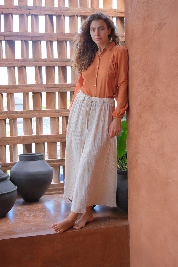 Introducing the Audrey X Crow Collection, featuring a woman in an orange Jane Austen Shirt and white skirt. This collection showcases hand-woven fabric with block-printed stripes, embodying elegance and artisanal craftsmanship. The vibrant orange and classic white combination adds a touch of sophistication to this beautifully crafted ensemble.