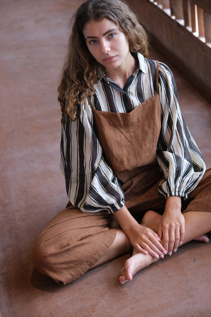 Introducing the Jane Austen Shirt from the Audrey X Crow Collection, elegantly worn by a woman in overalls. Seated on the floor, she effortlessly showcases the shirt's timeless design and refined craftsmanship